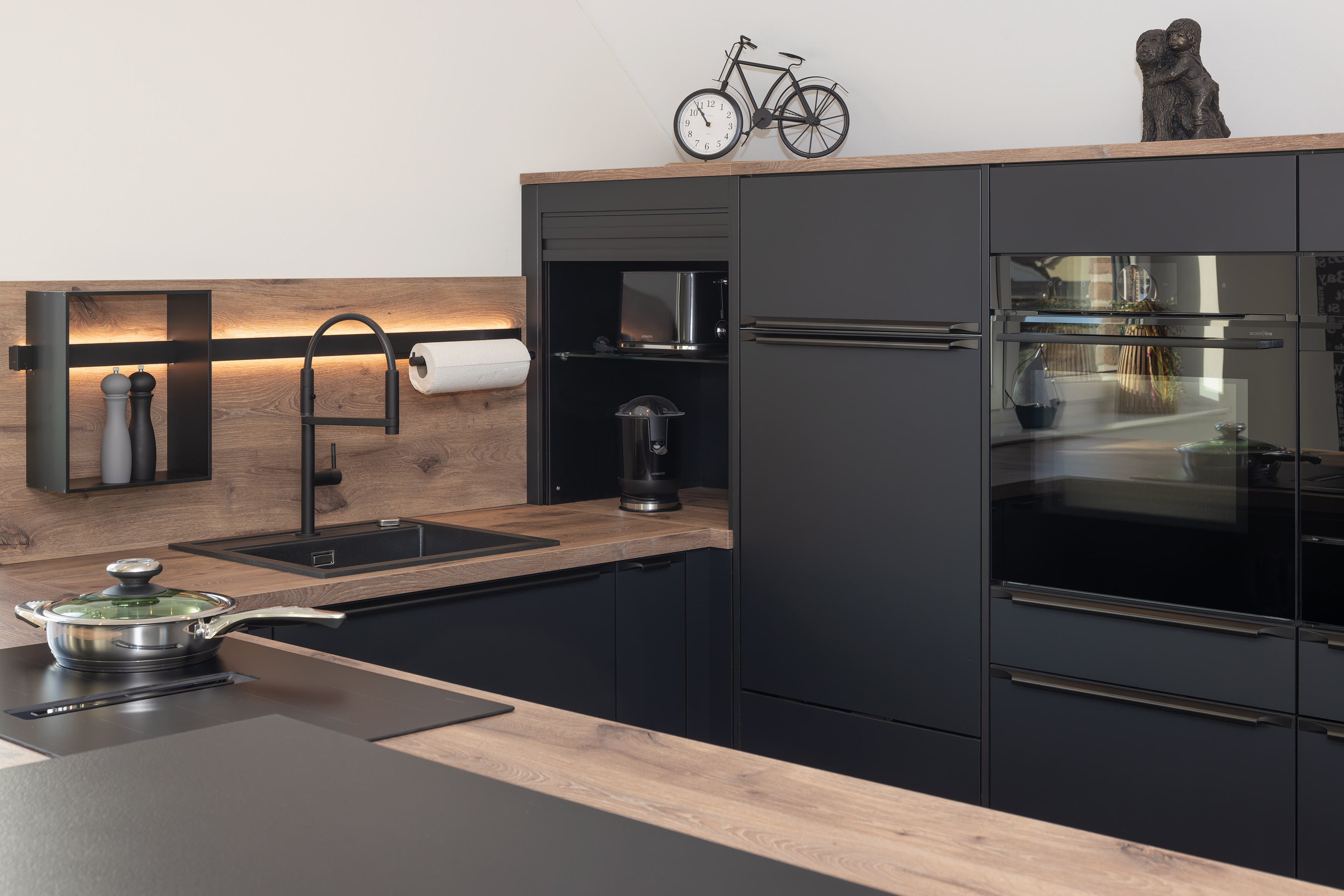 Moderne schwarze Küche mit Holzarbeitsplatte und eingebautem Ofen.