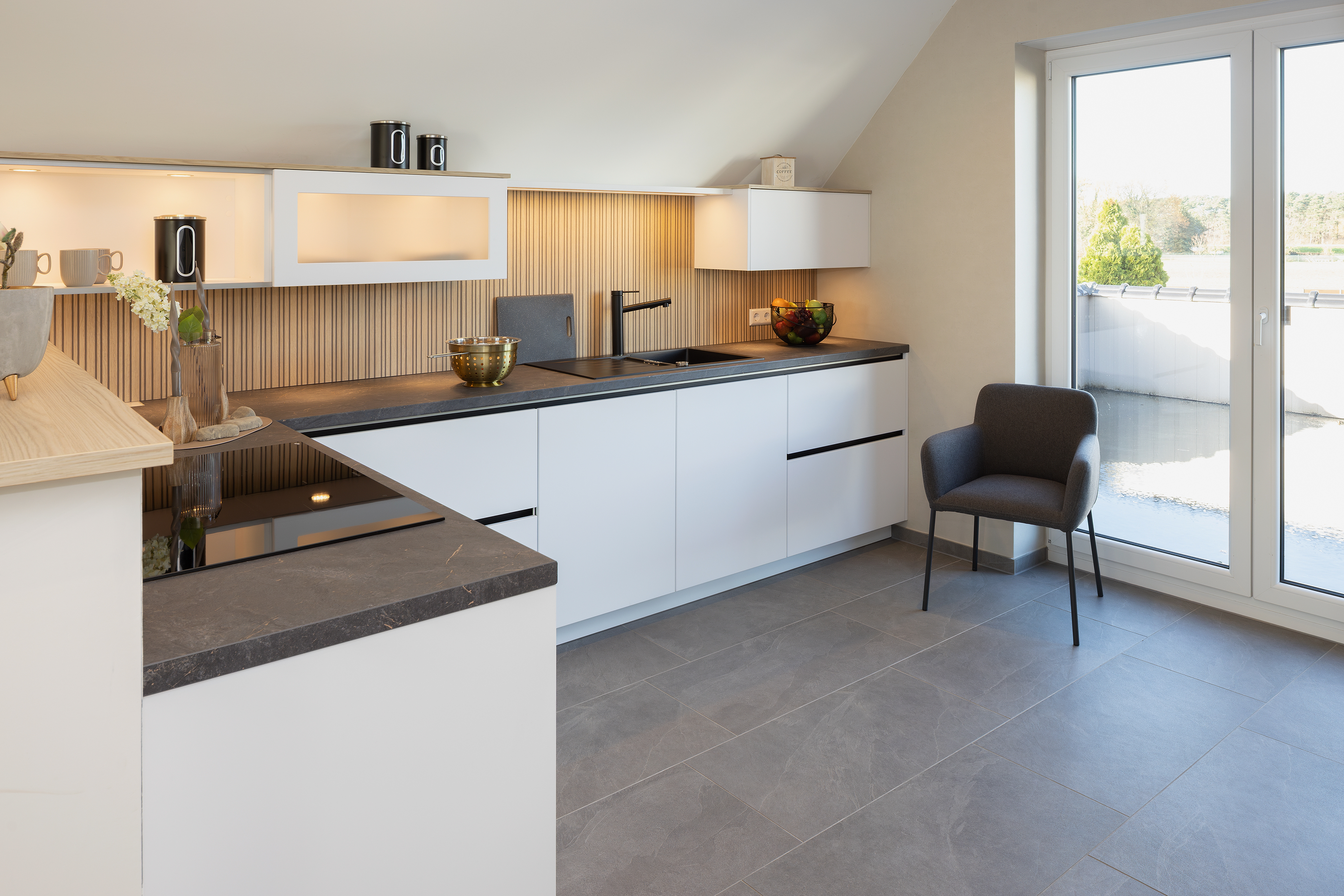 Moderne, helle Küche mit weißen Schränken, dunkler Arbeitsplatte und großem Fenster.