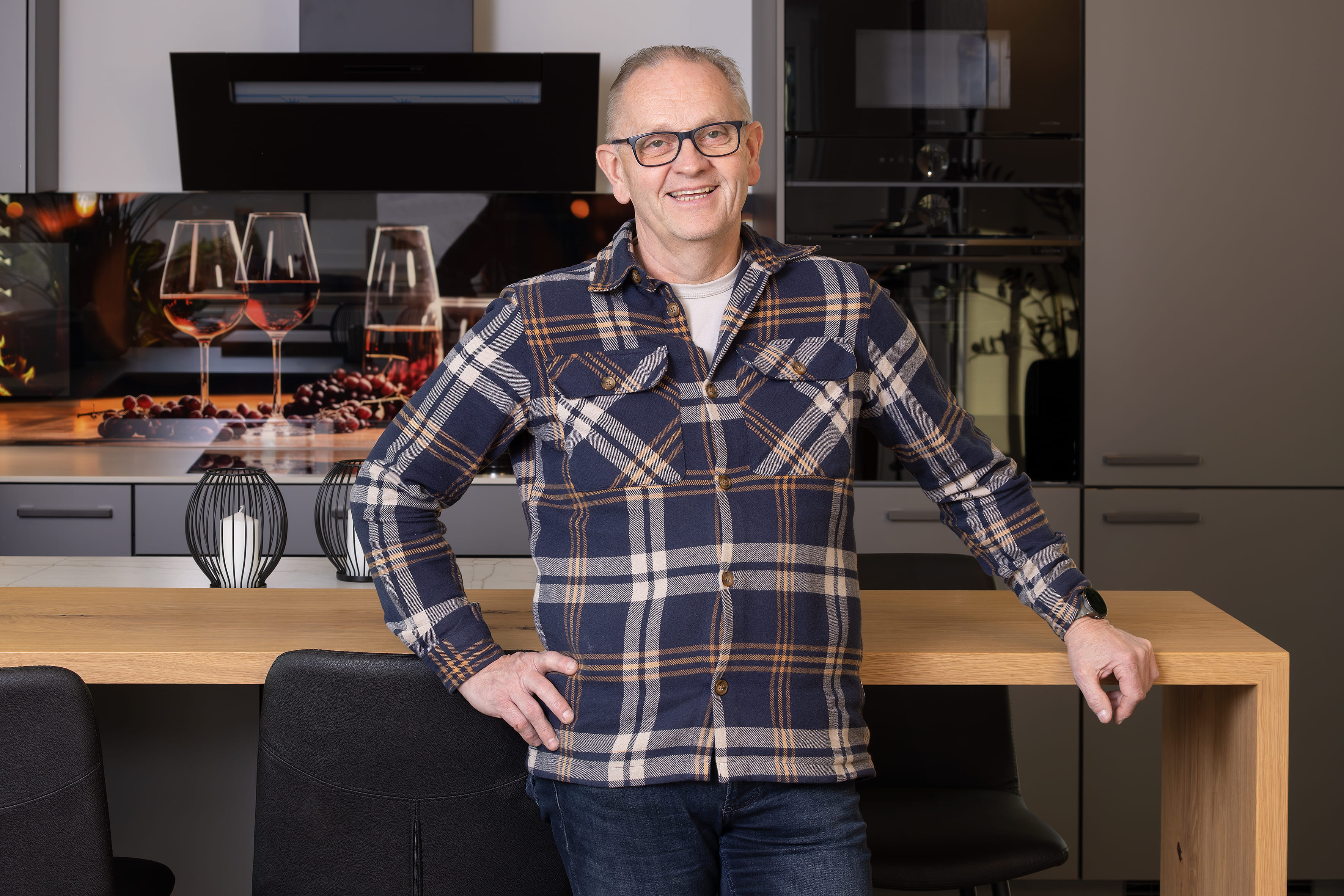 Herr Epkenhans. Mann mit Brille und kariertem Hemd steht lächelnd in moderner Küche.