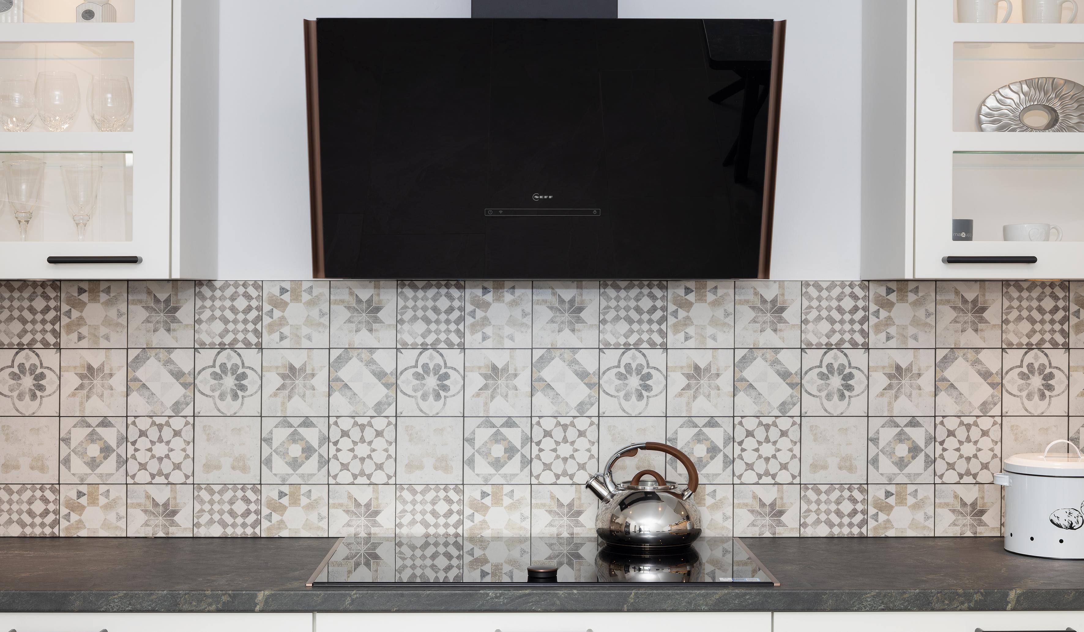 Moderne Küche mit gemusterten Fliesen, schwarzer Dunstabzugshaube und Teekessel auf dem Herd.