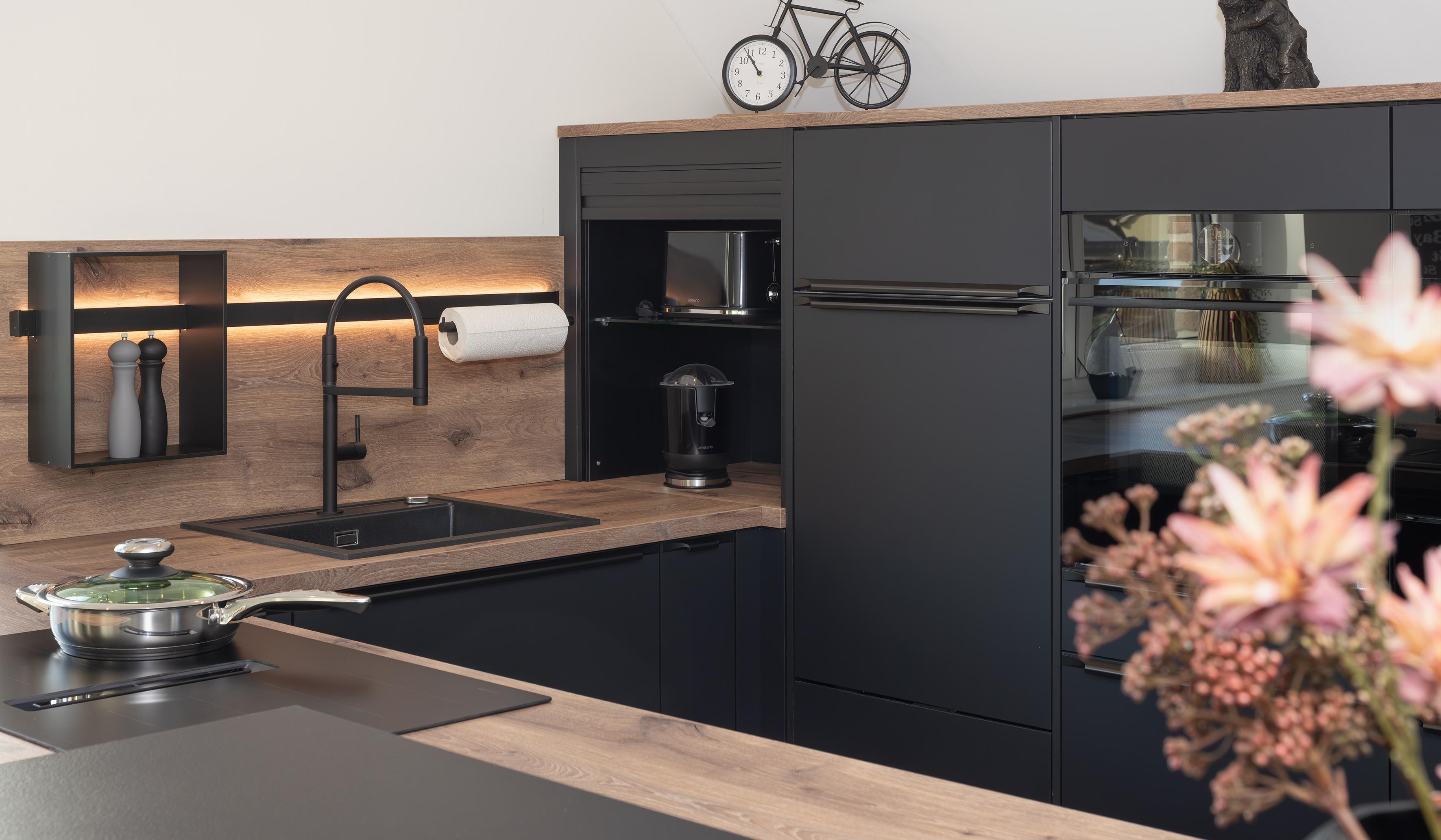 Moderne schwarze Küche mit Holzarbeitsplatte und stilvollen Dekorationen.