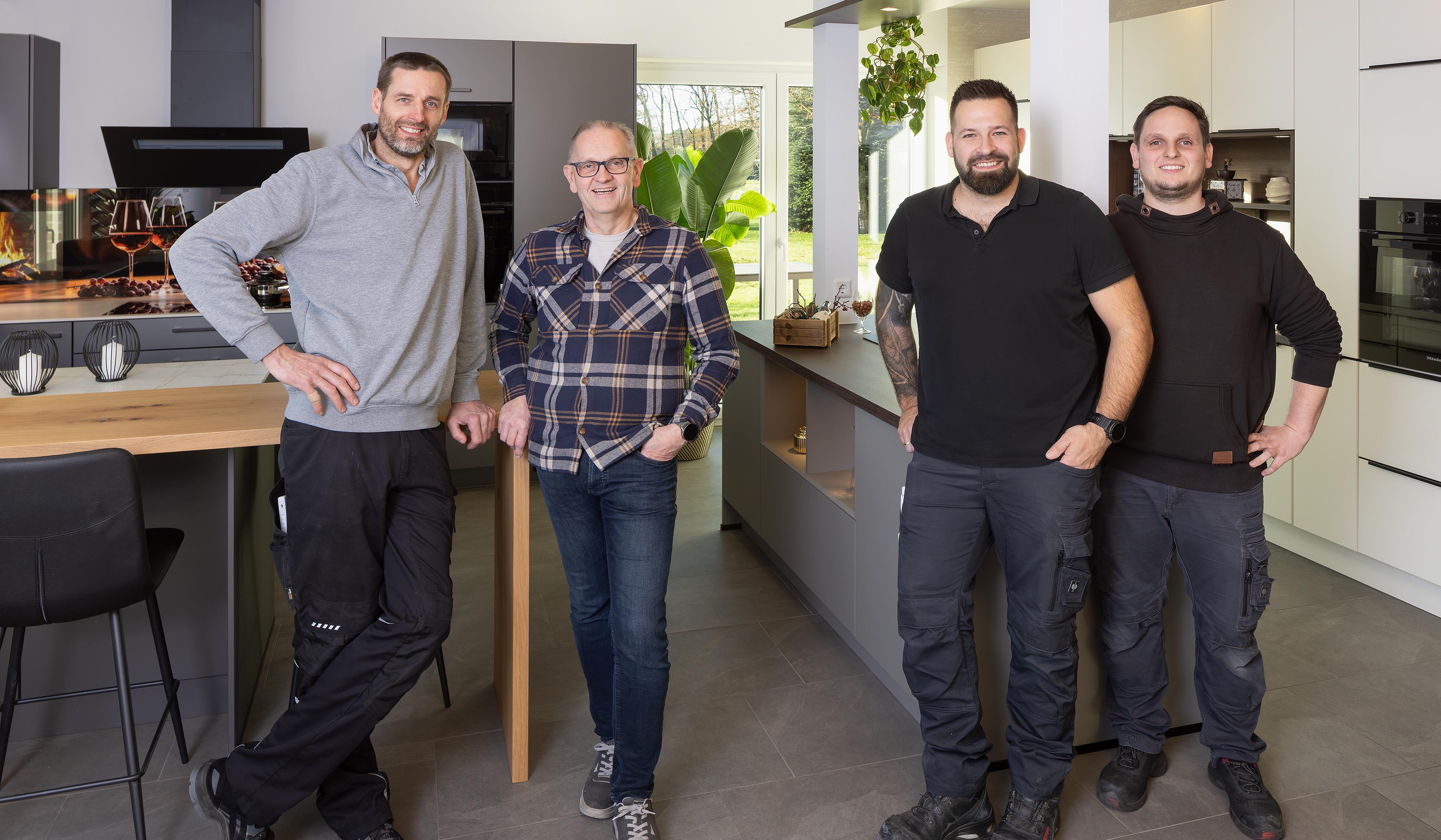 Vier Männer stehen lächelnd in einer modernen Küche.