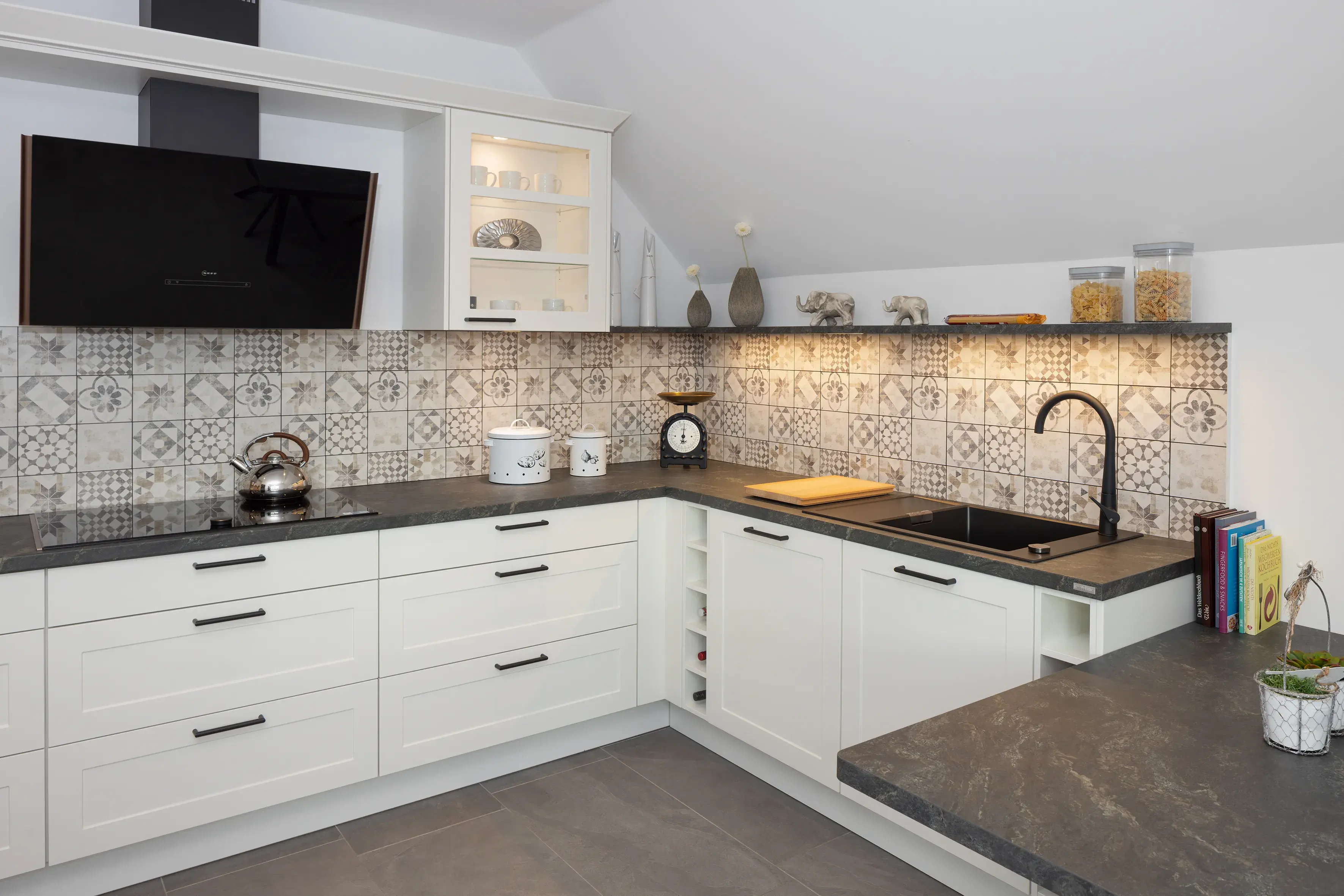 Moderne weiße Küche mit gemustertem Fliesenspiegel und dunkler Arbeitsplatte.