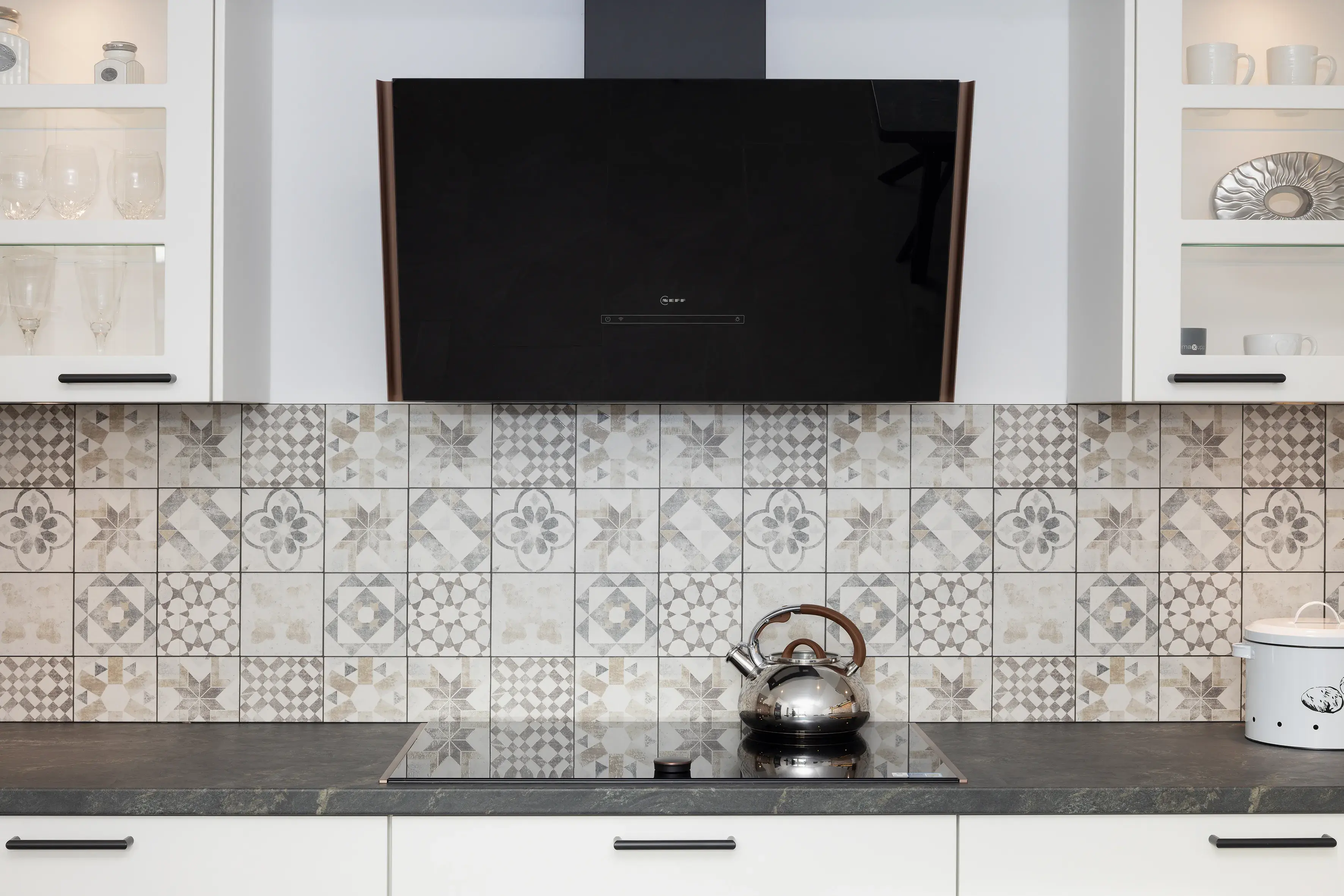 Moderne Küche mit gemusterten Fliesen, schwarzer Dunstabzugshaube und Teekessel auf dem Herd.