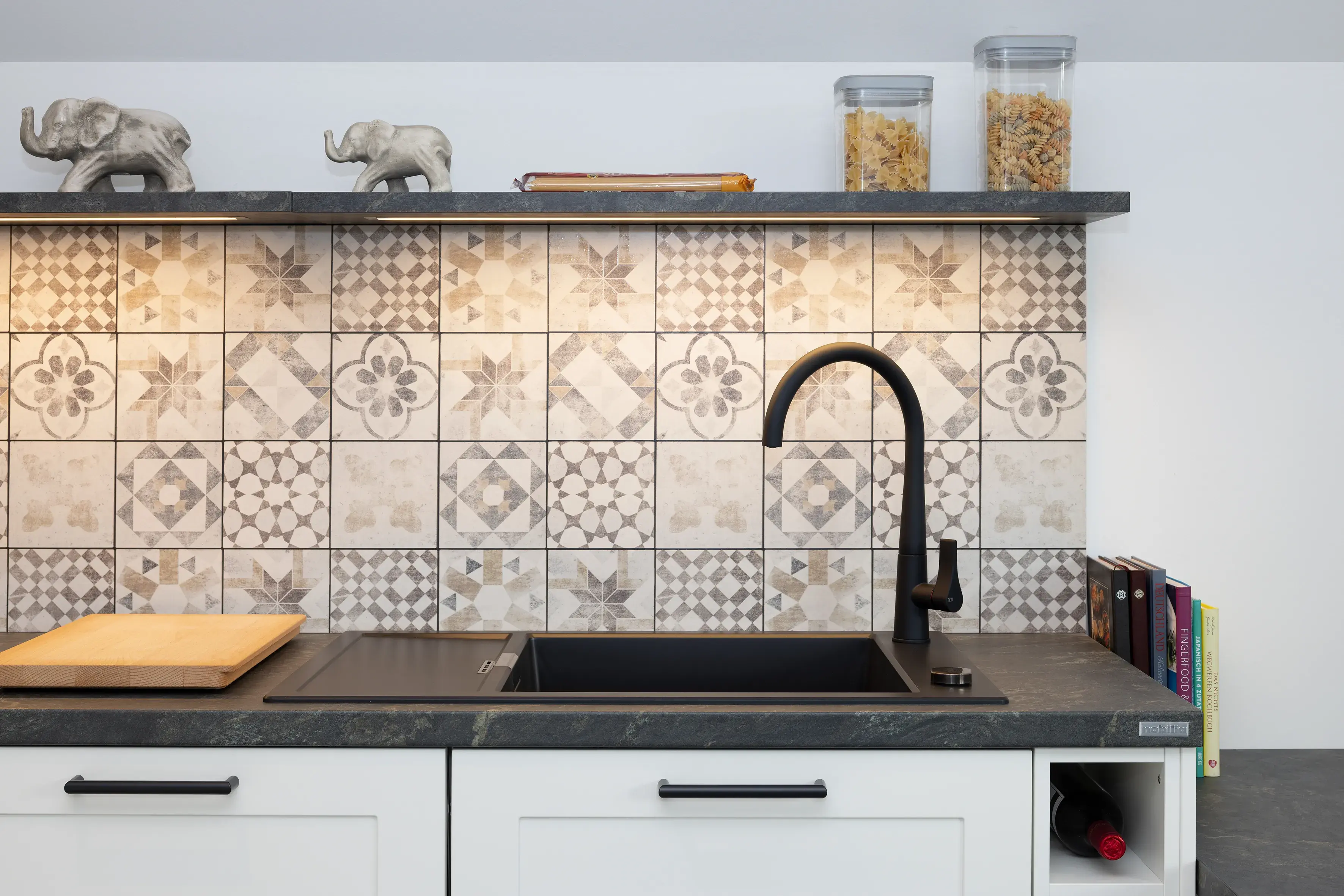 Moderne Küchenspüle mit gemusterten Fliesen, schwarzem Wasserhahn und Deko-Elefanten.