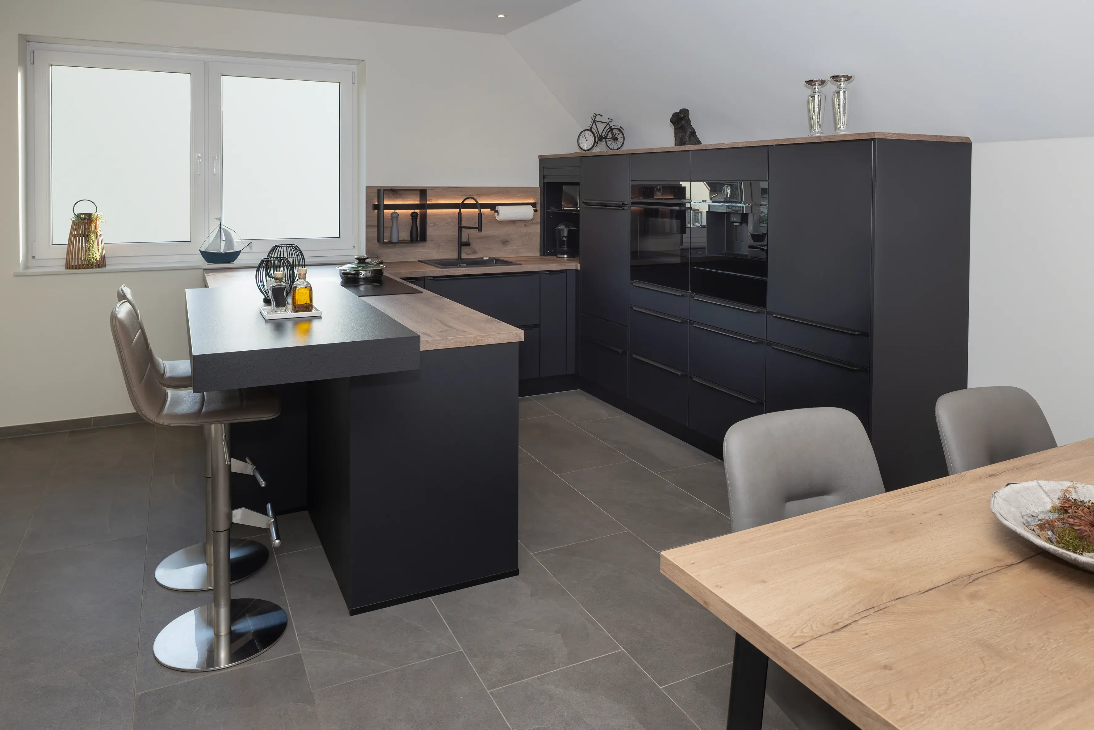 Moderne schwarze Einbauküche mit Holzarbeitsplatten und Esstisch, helle Fliesen.