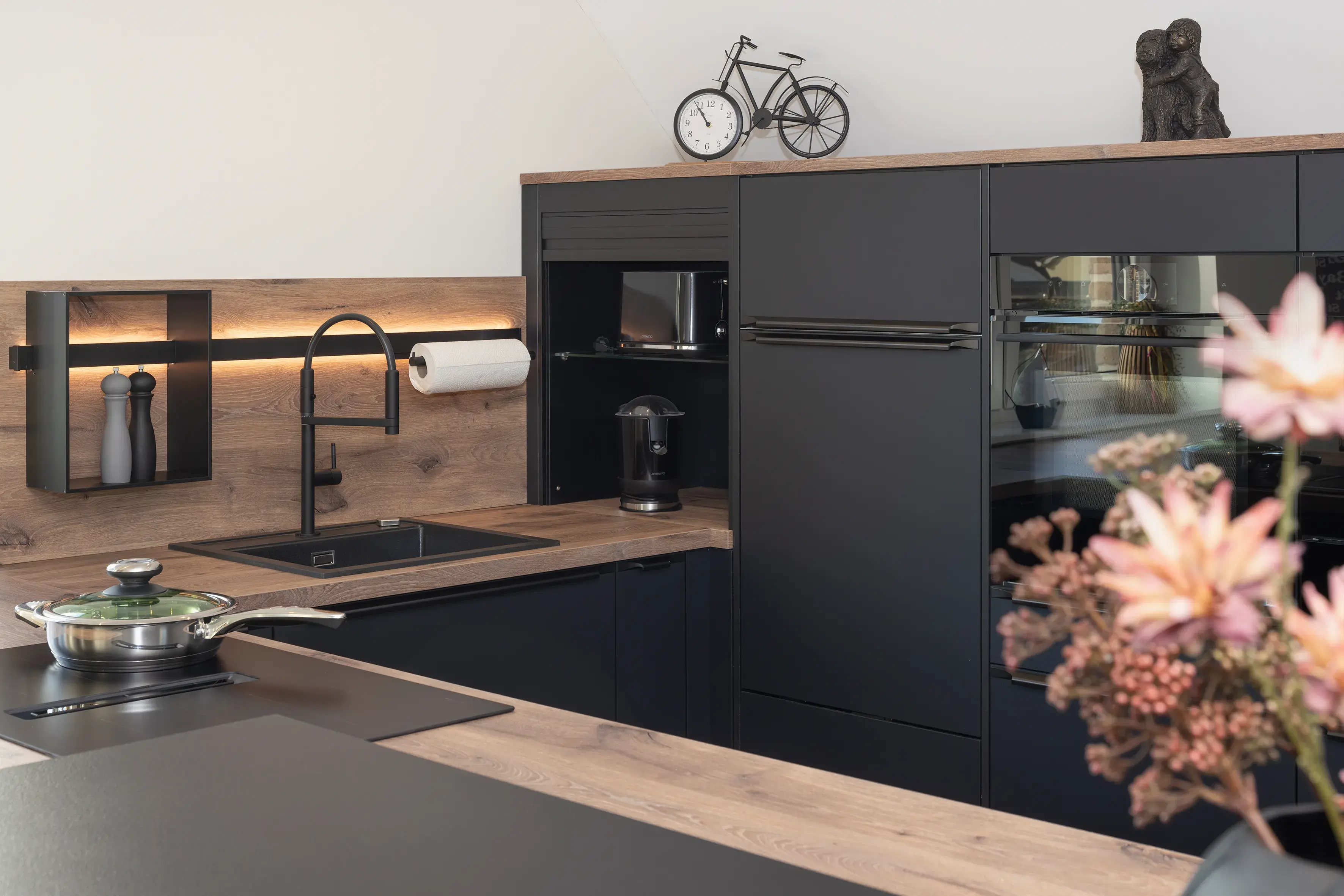 Moderne schwarze Küche mit Holzarbeitsplatte und stilvollen Dekorationen.