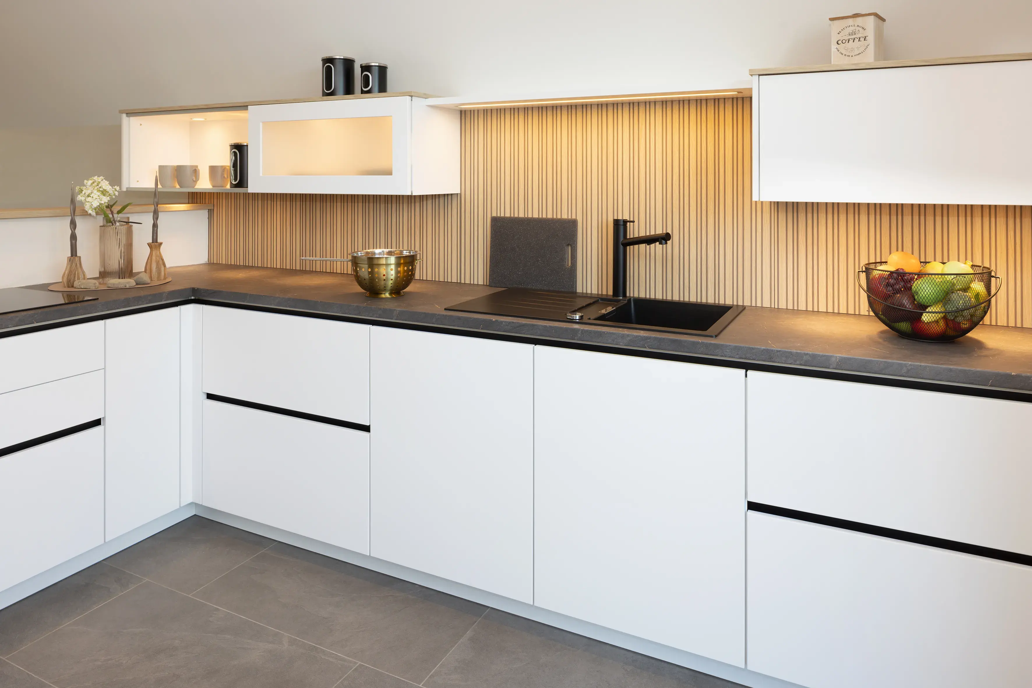 Moderne Küche mit weißen Schränken, dunkler Arbeitsplatte und Obstschale.