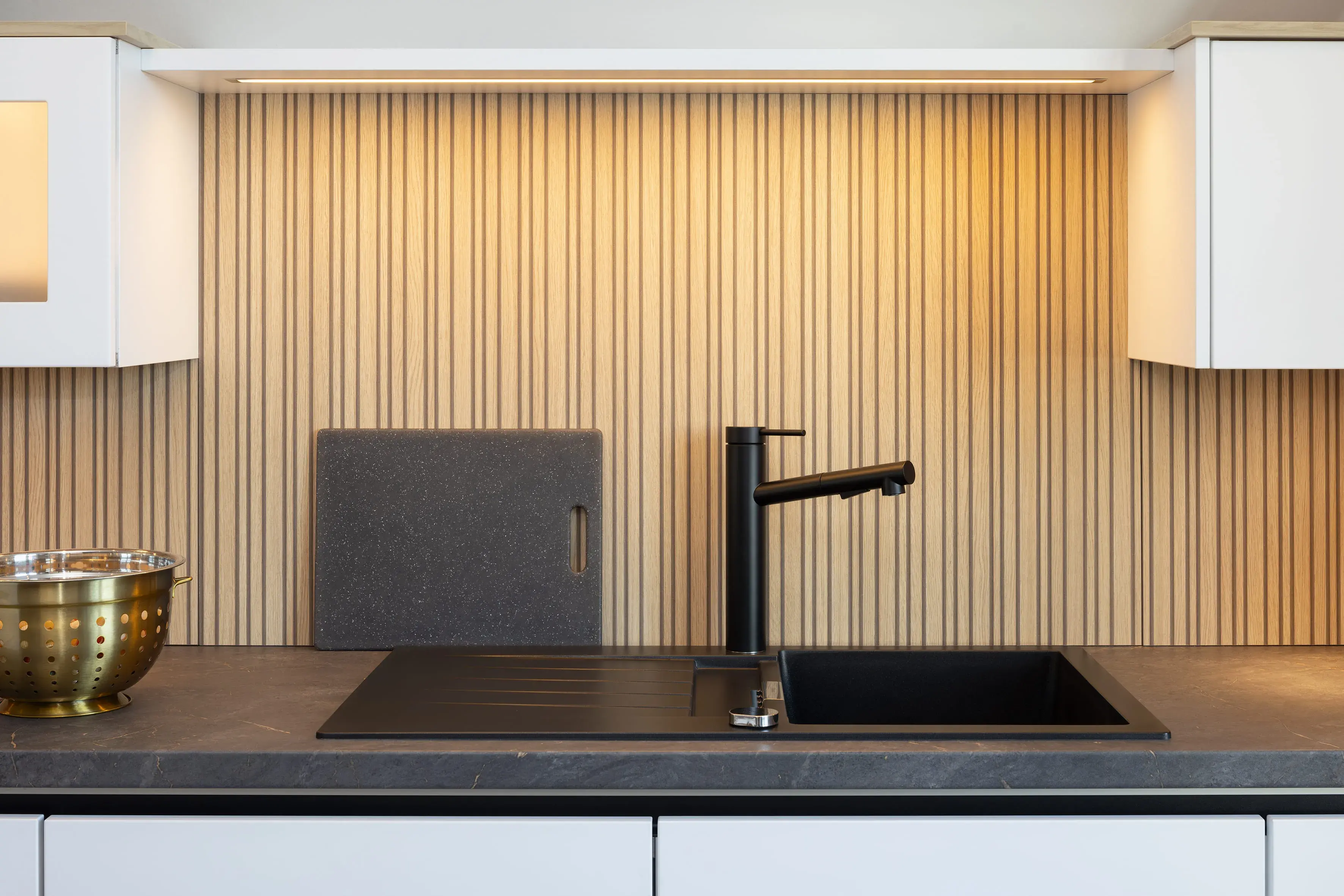 Moderne Küchenzeile mit schwarzer Spüle, Holzwand und Metallsieb