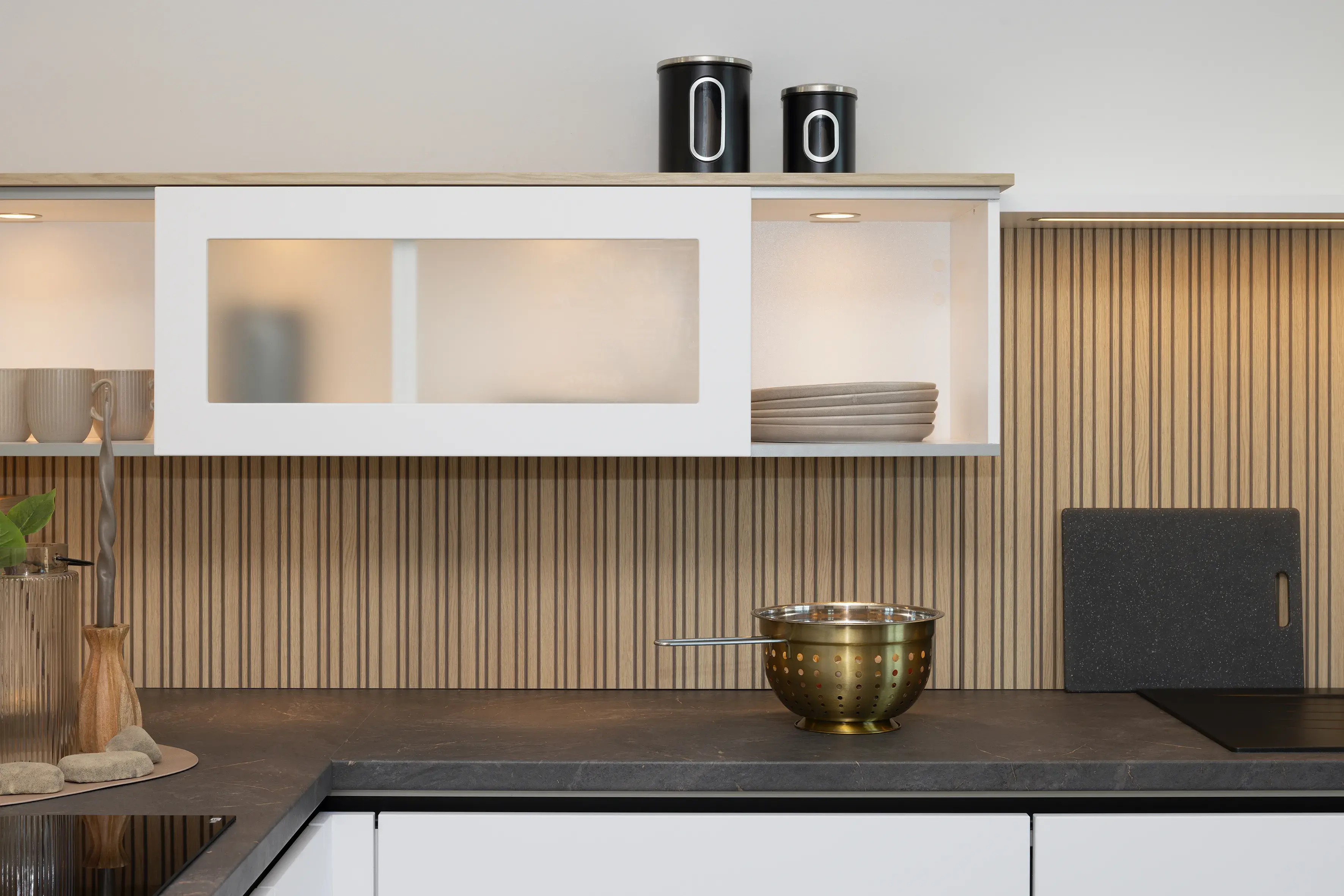 Moderne Küche mit Holzrückwand, goldener Schüssel und weißen Hängeschränken