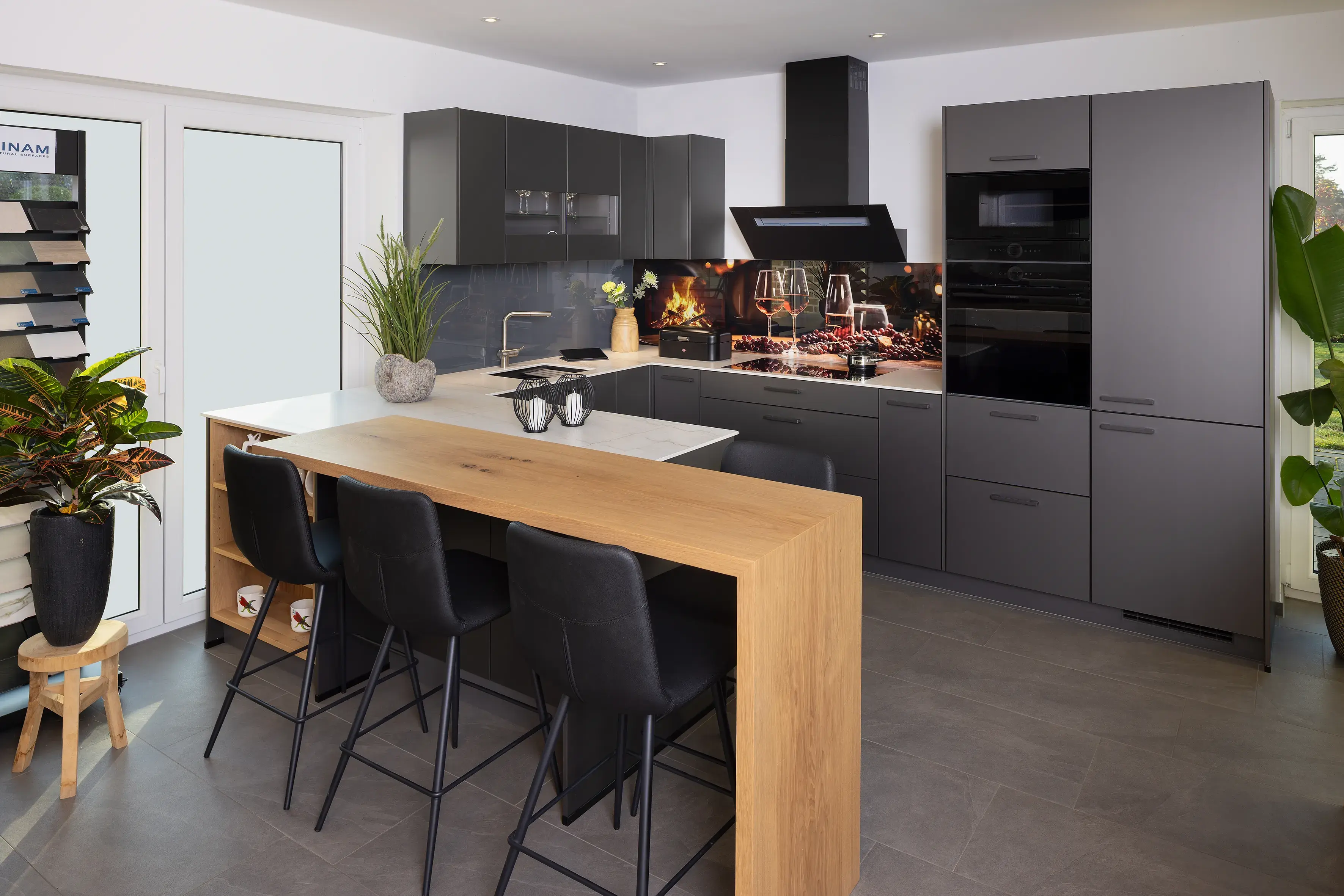 Moderne Küche mit grauen Schränken, Holztheke und schwarzen Barhockern.