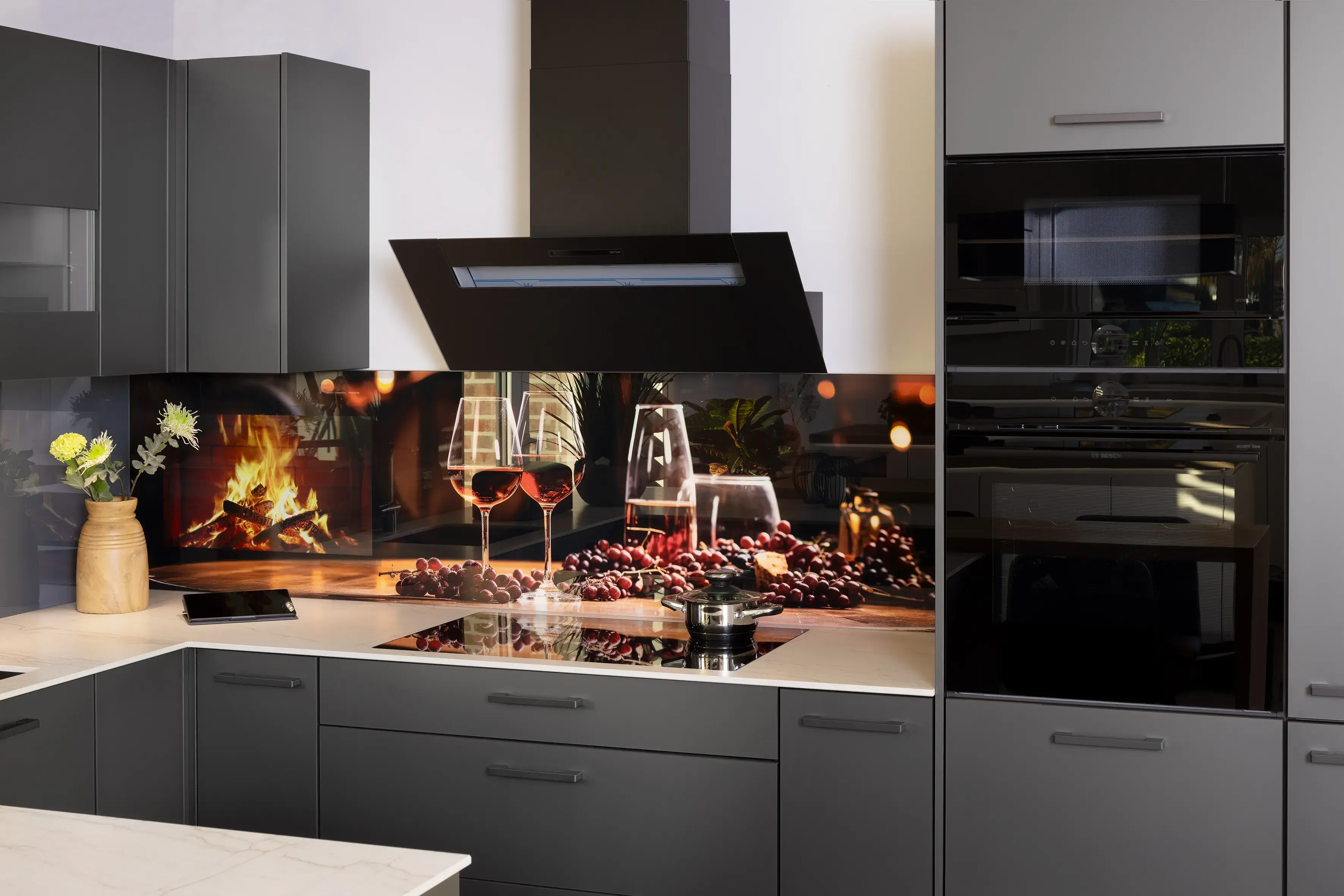 Moderne graue Küche, Kochfeld, Kaminbild mit Weingläsern als Rückwand.