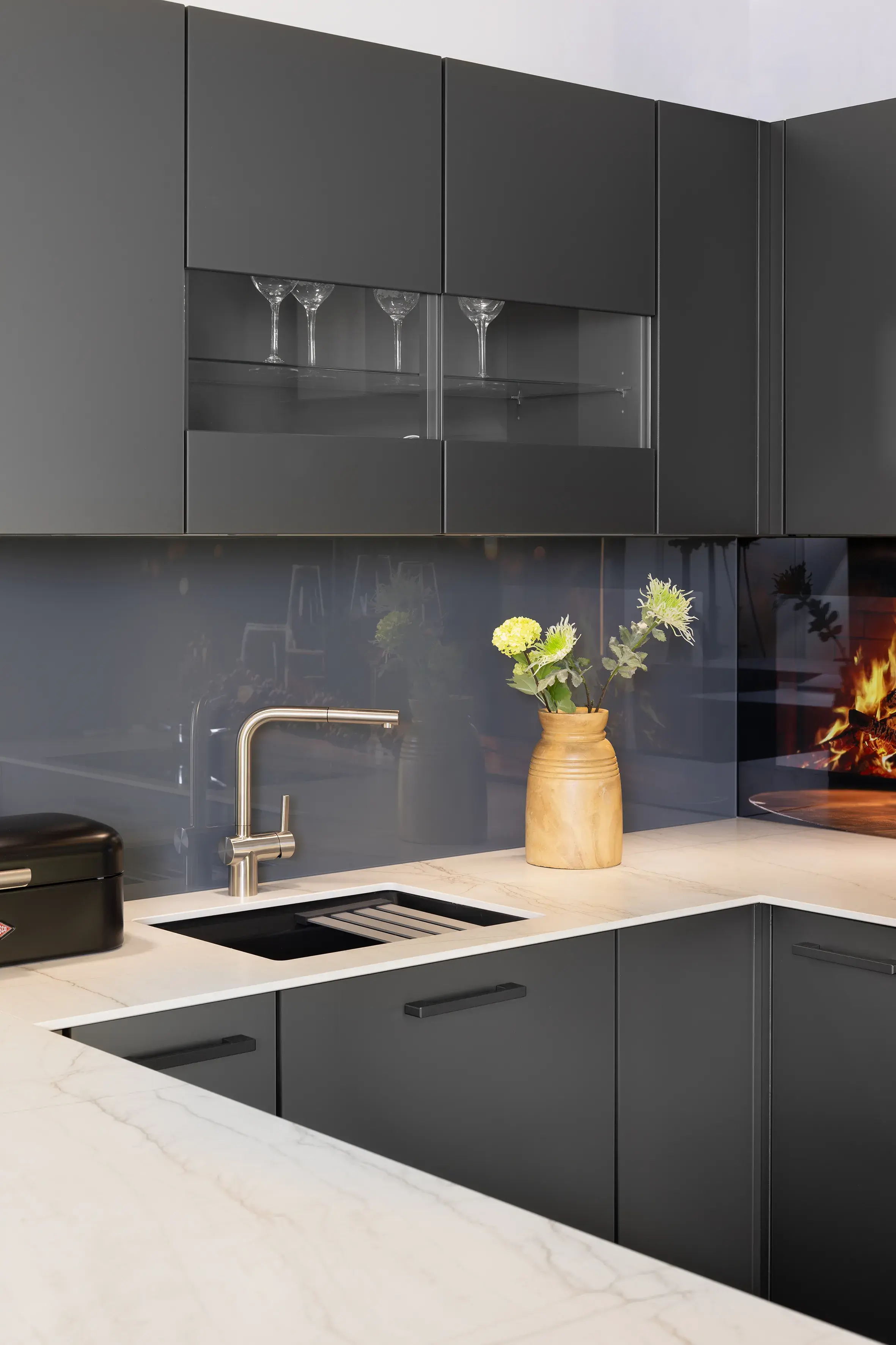 Moderne Küche mit dunklen Schränken, Marmorarbeitsplatte und Vase mit gelben Blumen