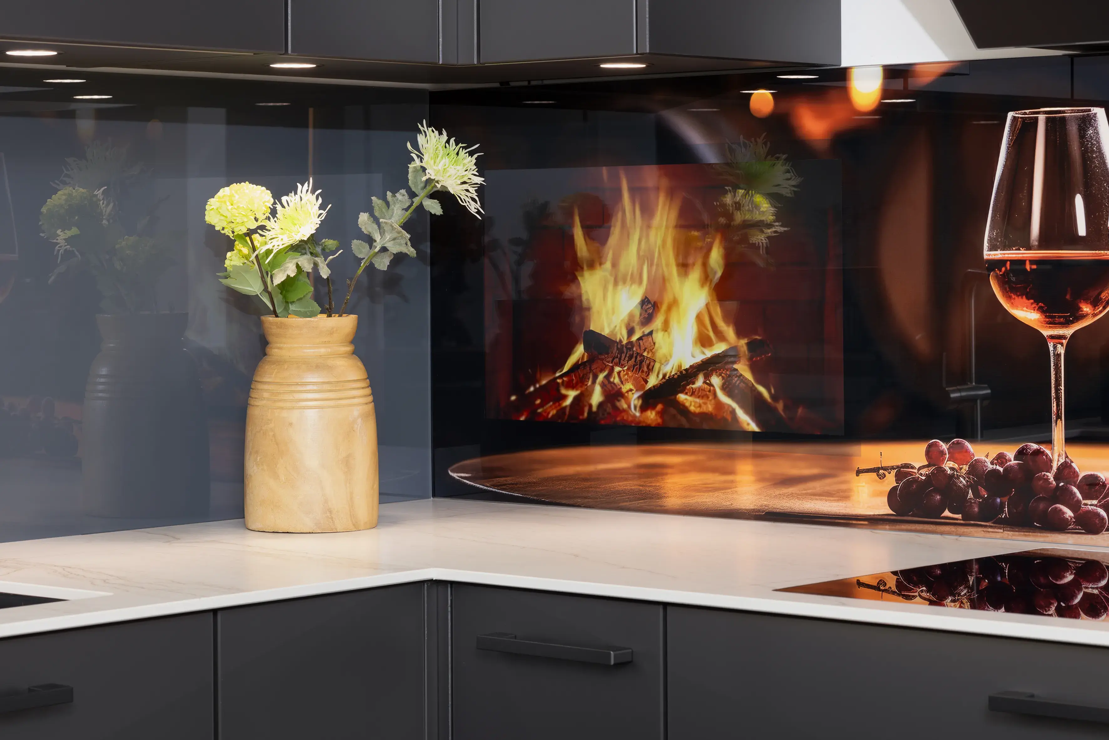 Moderne Küche mit Vase, Blumen, Weinglas, Trauben und Kaminbild auf einer Rückwand.