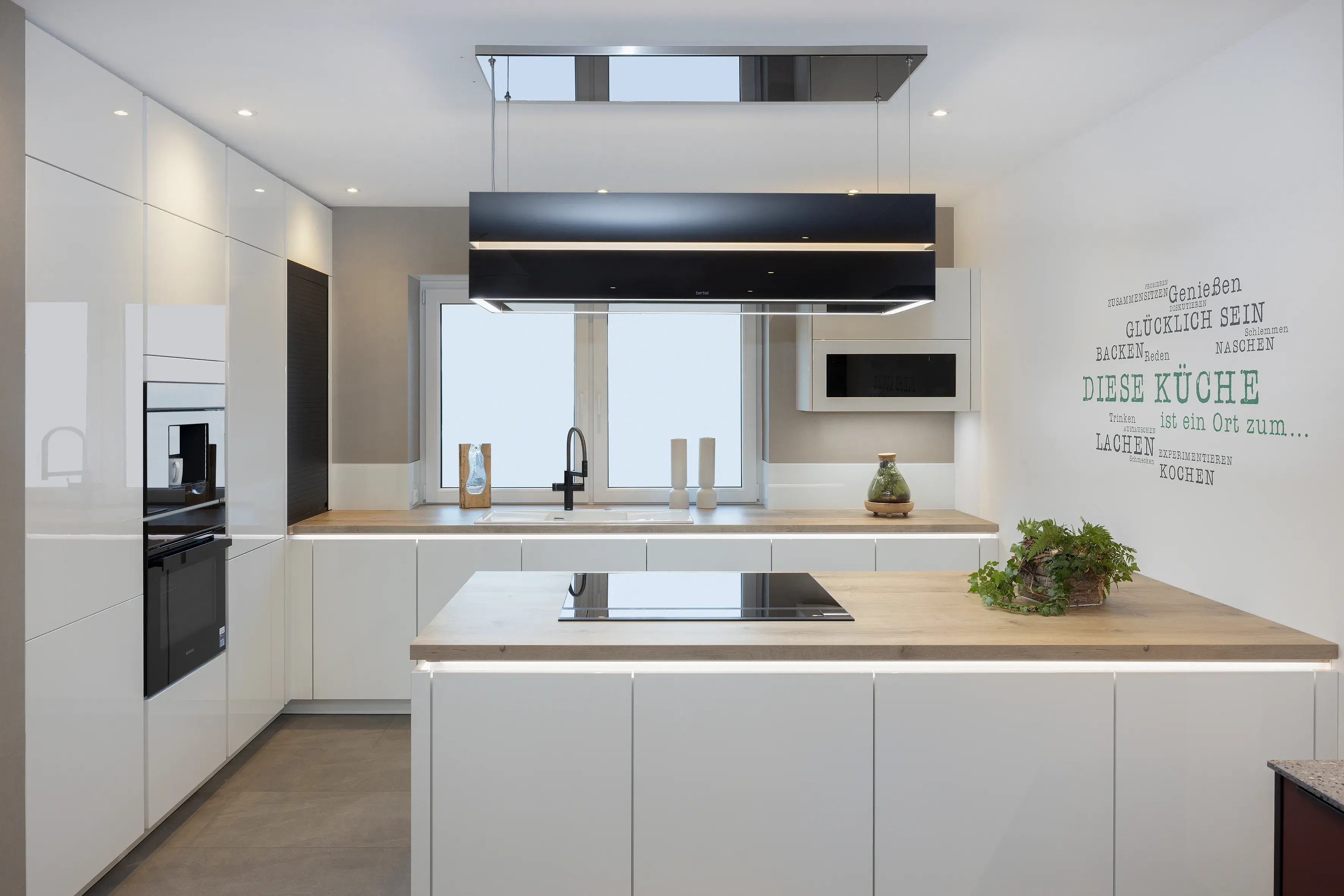 Moderne weiße Küche mit Holzarbeitsplatte, Kochfeld und Pflanzen.